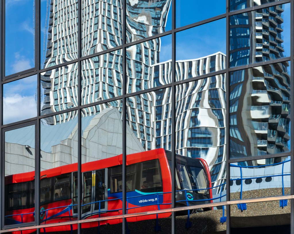 Reflections of a red DLR train in a Canary Wharf office window